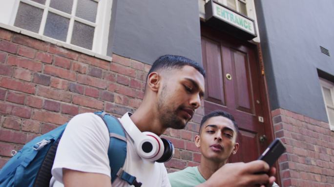 两个混血男性朋友在街上坐着、聊天、使用智能手机