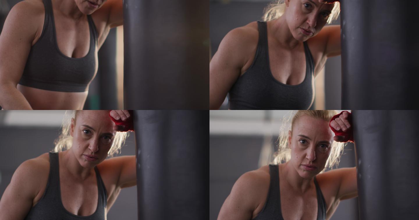 白人女拳击手的肖像靠在拳击袋在健身房