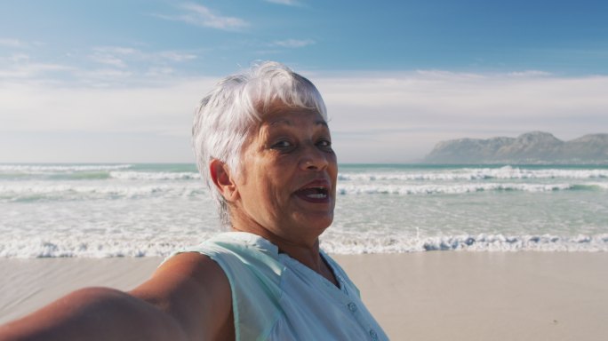一位年长的非洲裔美国妇女对着镜头微笑，在海滩上散步