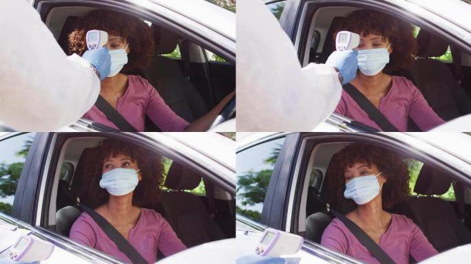 非裔美国妇女戴着口罩坐在车里，由医护人员测量体温