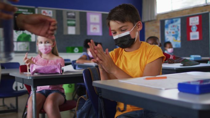 混血儿学生戴着口罩在教室里消毒双手，同事们在后台