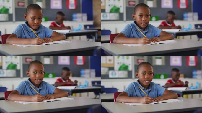 快乐的非裔美国学生的肖像坐在教室里，做笔记，看着相机