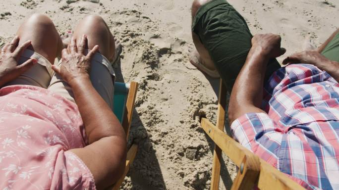 老年非洲裔美国夫妇坐在沙滩上，手牵着手