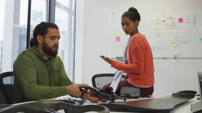 混合种族的男性和女性商业同事持有无人机和平板电脑在会议室