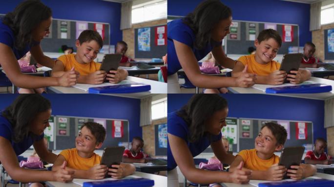 多样的微笑的女老师帮助坐在教室里的男孩，使用平板电脑