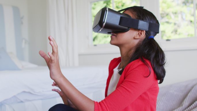 混血女孩坐在家里的沙发上玩戴着虚拟现实眼镜