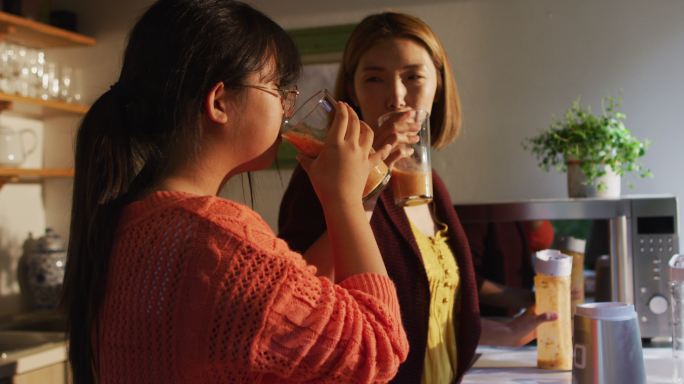 亚洲母女在厨房里喝着健康的饮料笑着