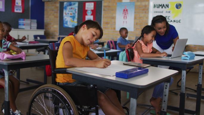 一个坐着轮椅的混血男孩，坐在教室里做笔记，背景里是老师