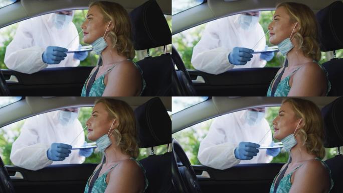 白人女性坐在车里，戴着口罩，在户外接受医务人员的新冠病毒检测