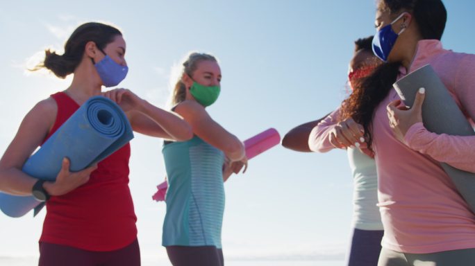 一群戴着口罩、拿着瑜伽垫、手肘触碰的女性朋友