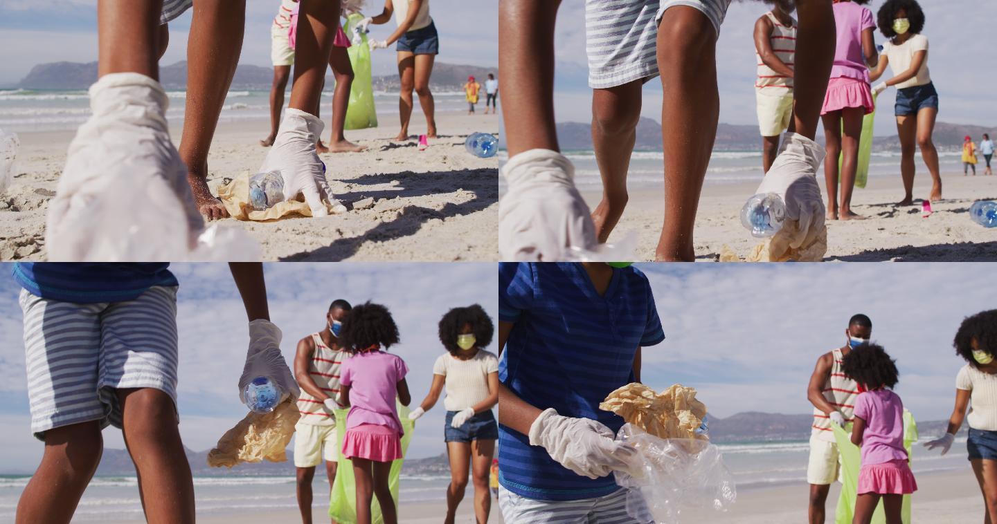非裔美国父母带着两个戴口罩的孩子在海滩上捡拾垃圾