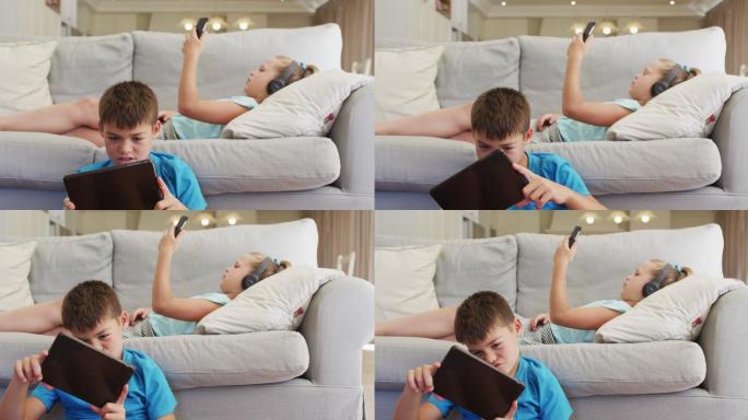 白种人兄妹用平板电脑和智能手机躺在沙发上的照片