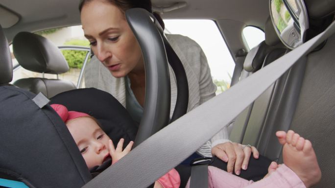 一位白人母亲在车里的安全座椅上亲吻她的孩子