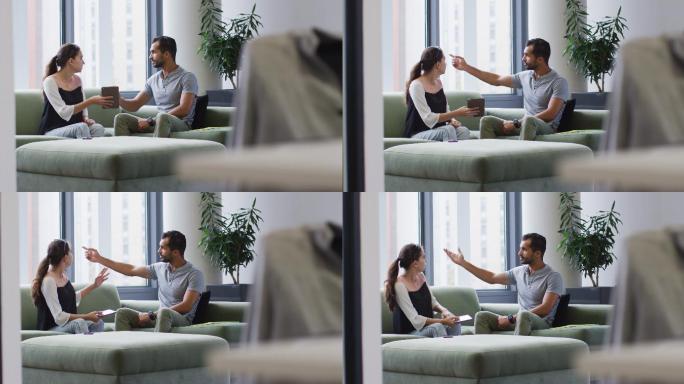不同的男男女女同事坐在沙发上看着平板电脑聊天