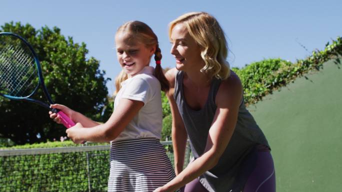 一个白人母亲在一个阳光明媚的日子在教她的女儿打网球