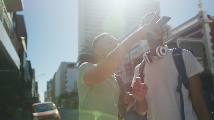 两个快乐的混血男性朋友站在街上聊天，使用智能手机