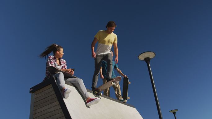快乐的白种人女人和两个男性朋友在阳光灿烂的日子玩滑板