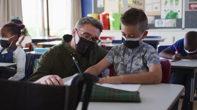 男老师坐在教室里帮助男生，都戴着口罩