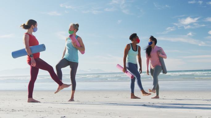 一群戴着口罩、拿着瑜伽垫在沙滩上的女性朋友