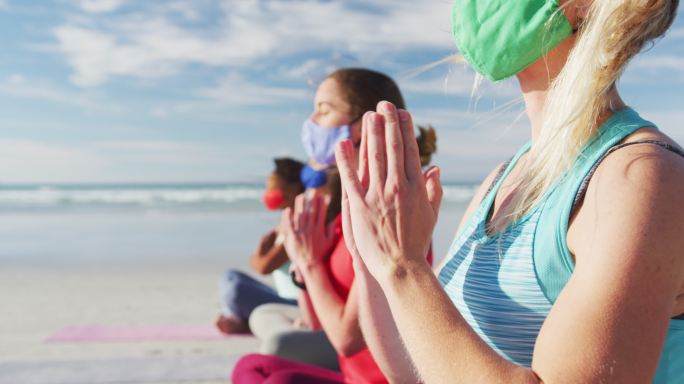 一群女性朋友戴着口罩在海滩上冥想