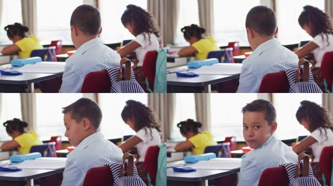 肖像快乐的混血男孩坐在教室，做笔记，看着相机