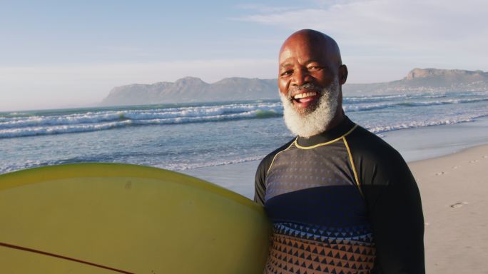 微笑的资深非洲裔美国人走在海滩冲浪板