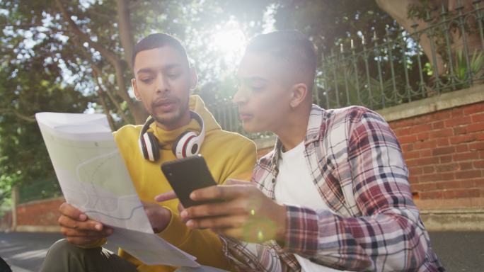 两个快乐的混血男性朋友坐着，玩着智能手机和地图