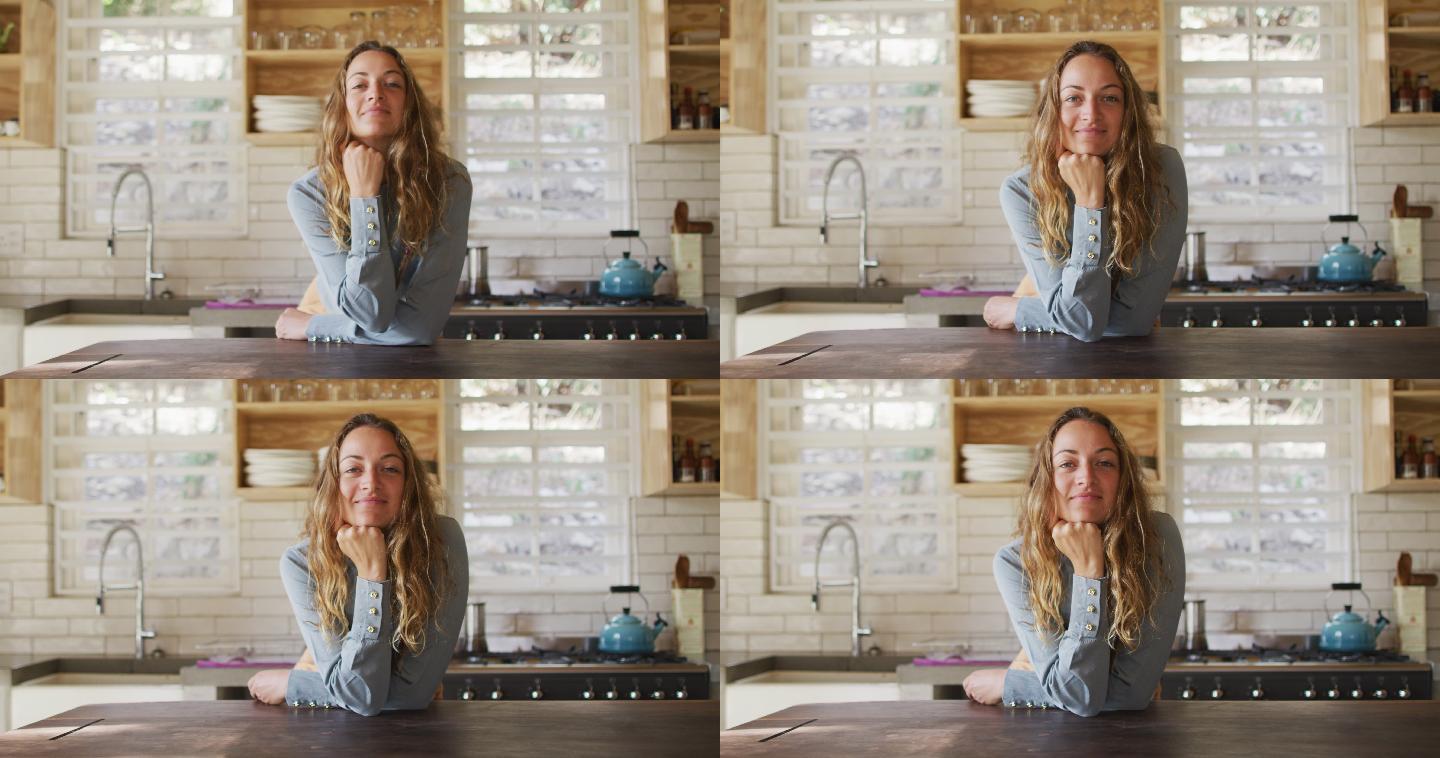 快乐的白人妇女的肖像，站在阳光明媚的小屋厨房里，倚在柜台上