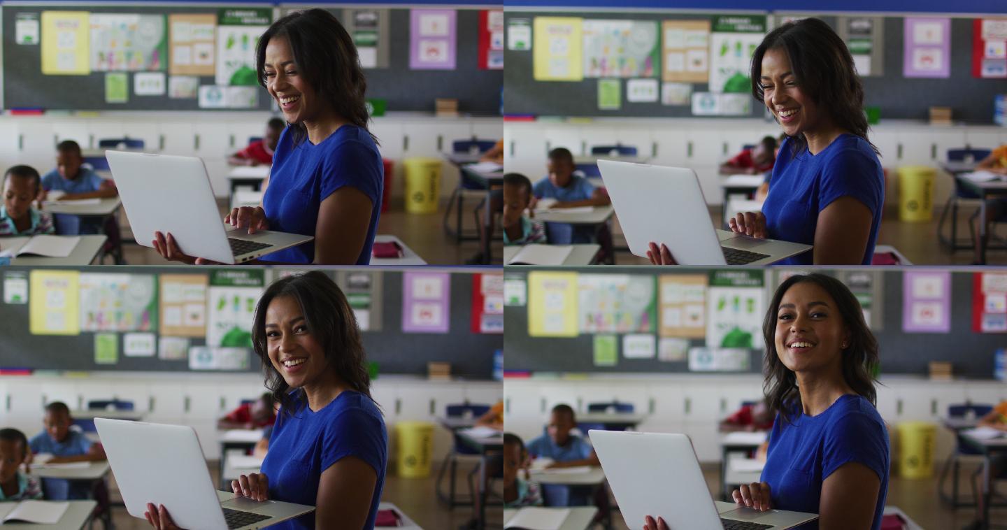 快乐的混血女教师的肖像站在教室里，背景是笔记本电脑的孩子们