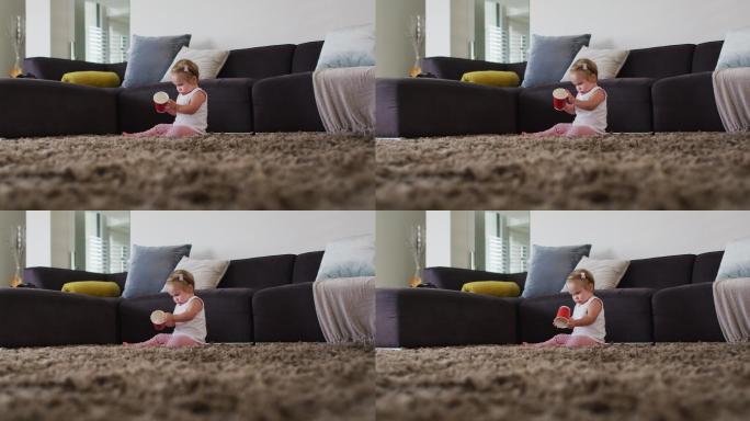 一个白人婴儿坐在家里的地板上玩塑料杯