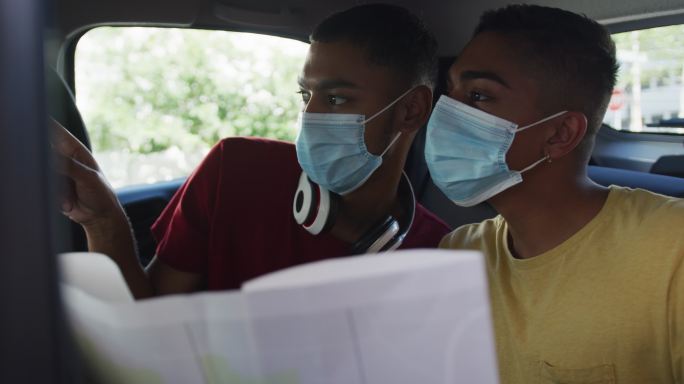 两个混血男性朋友戴着口罩在出租车上使用地图