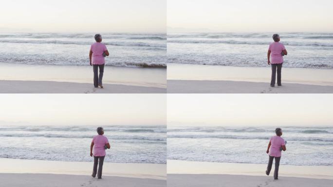 非裔美国高级妇女持有瑜伽垫看着海浪，而站在海滩上