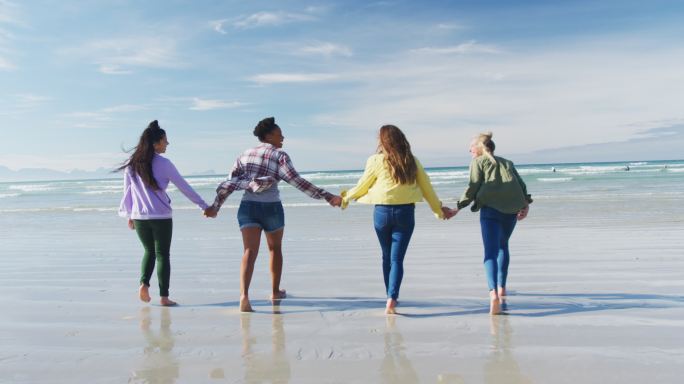 快乐的一群不同的女性朋友玩得开心，在沙滩上牵着手散步