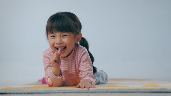 快乐的小女孩趴在地毯上吃棒棒糖