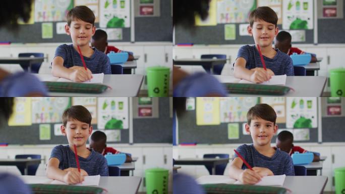 快乐的白人男孩的肖像坐在教室里，做笔记，看着相机