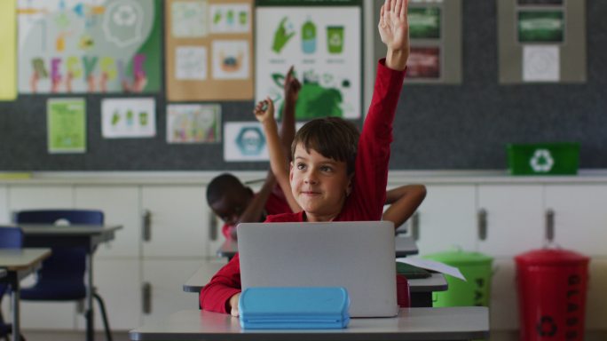 快乐的白人学生肖像与笔记本电脑坐着举起手回答问题