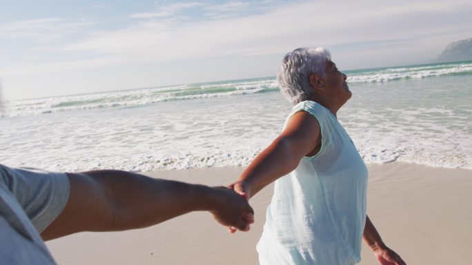 一对非洲裔美国老夫妇在海滩上手牵着手散步