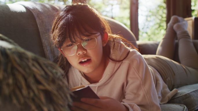 亚洲女孩微笑着坐在家里的沙发上看书