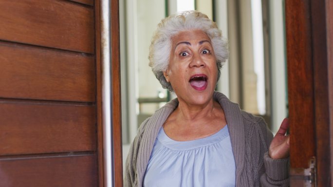 非裔美国老年妇女打开前门欢迎回家的画像