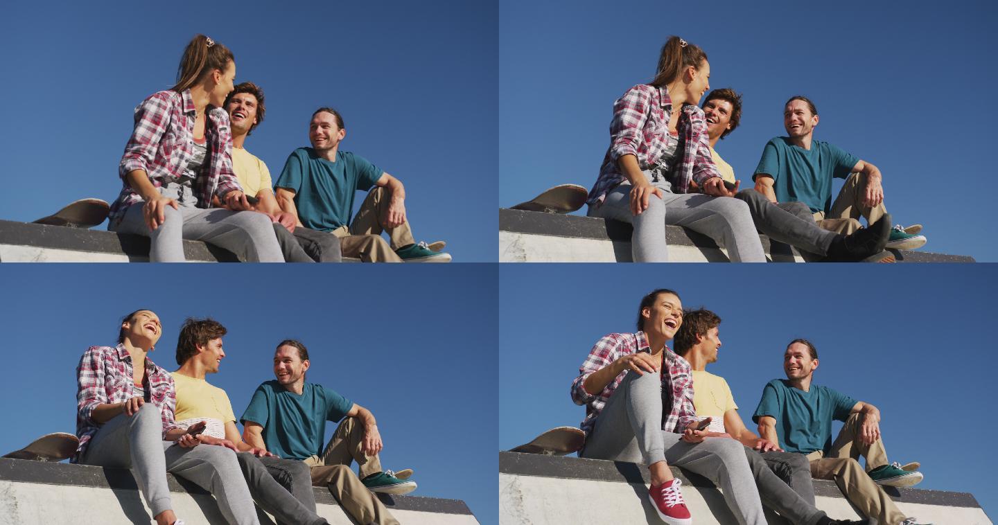快乐的白种人女人和两个男性朋友坐在一起，在阳光灿烂的日子里一起欢笑