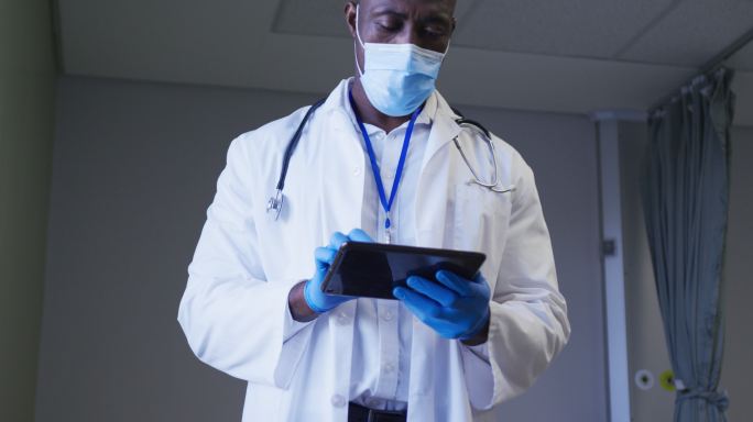 非裔美国男医生戴着口罩在医院病房使用数码平板电脑