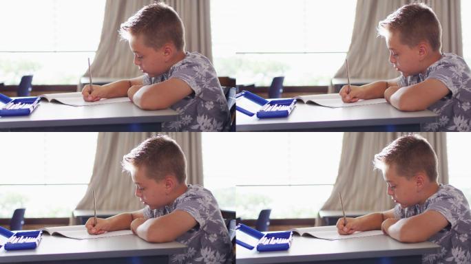 快乐的白人男孩的肖像坐在教室里，做笔记，看着相机