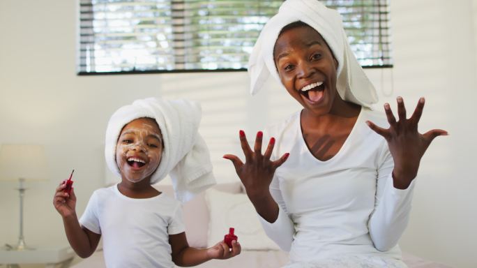 快乐的非裔美国母亲和女儿坐在床上，向镜头展示涂过的指甲