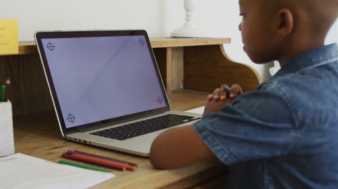 一个非裔美国男孩在网上学校的课堂上使用笔记本电脑，屏幕上有拷贝空间