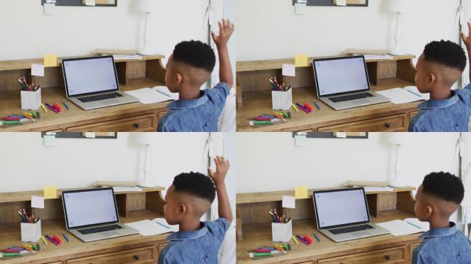 一个非裔美国男孩在网上学校的课堂上举起手，在屏幕上使用笔记本电脑的拷贝空间