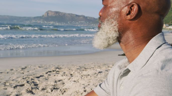 一位年长的非洲裔美国人坐在沙滩上，欣赏着风景