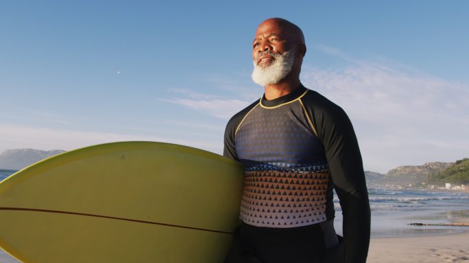 一位年长的非洲裔美国人在海滩上用冲浪板行走