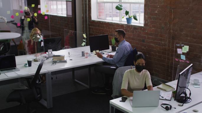 各种各样的男性和女性同事戴着口罩，用笔记本电脑和智能手机通话