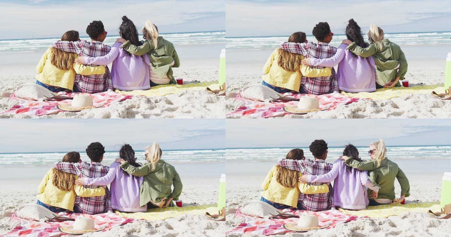 一群快乐的女性朋友，坐在毯子上，拥抱在沙滩上