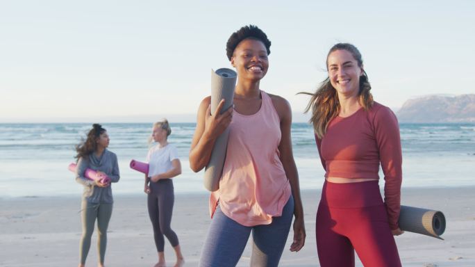 一群不同类型的女性朋友在沙滩上拿着瑜伽垫